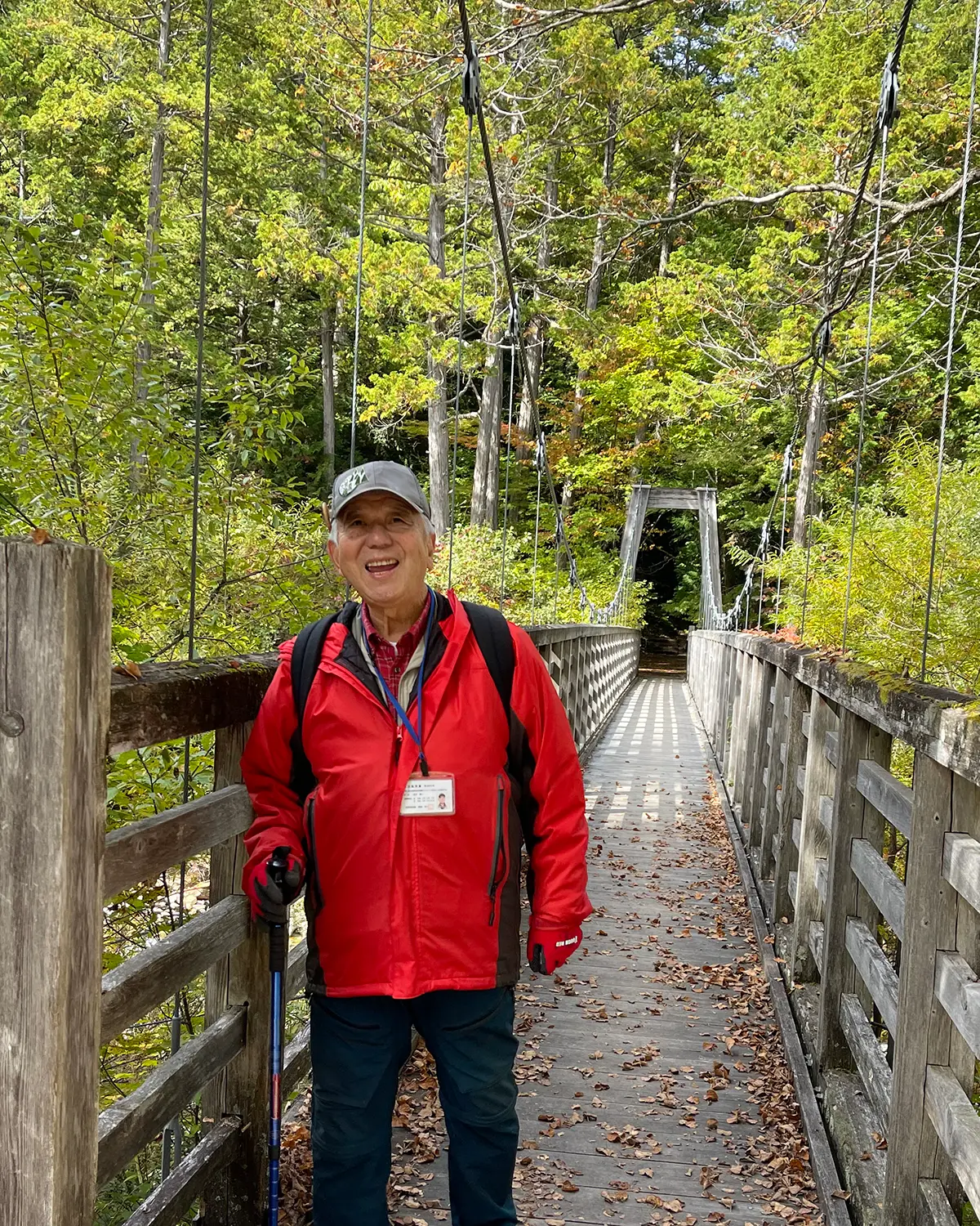 A member of a recent forest therapy session & trail guide experience smiling on a trail with a walking bridge