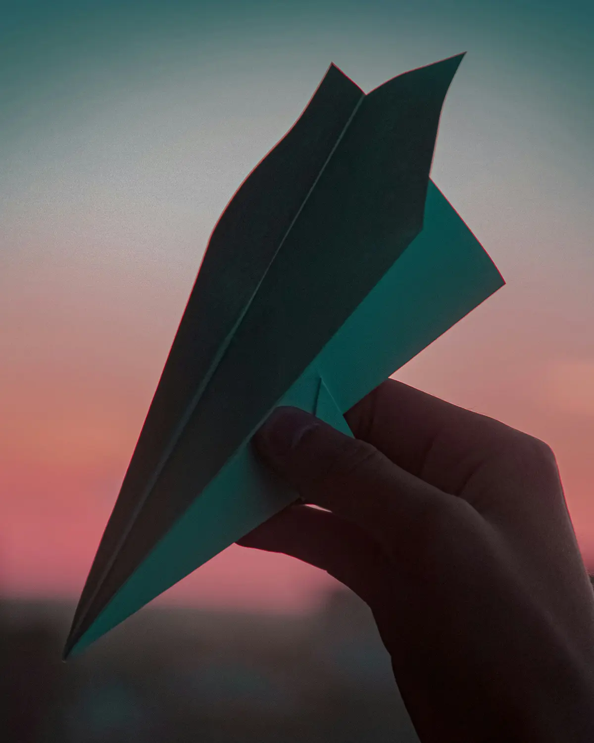 Silhouette of a person's hand during dusk, holding a paper place (metaphor for contacting someone)